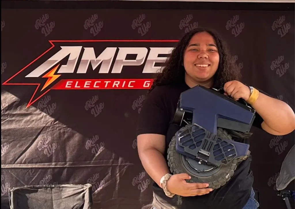 Sydnie holding a blue electric unicycle in front of an Amped backdrop